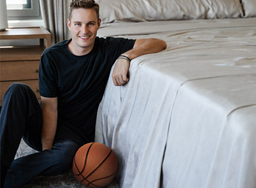 Sam Merrill sitting by a bed with Cariloha sheets