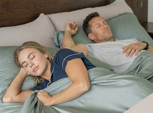 a man and woman sleeping in a bed with bamboo bed sheets