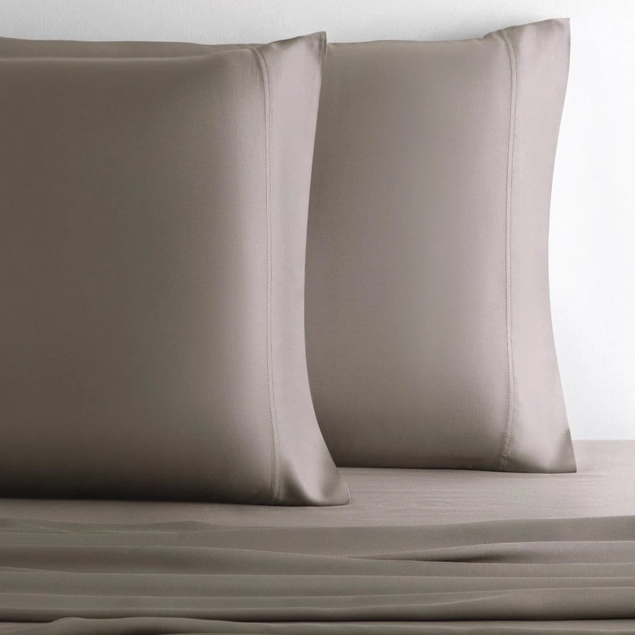 Two taupe satin pillowcases resting on a matching taupe sheet against a plain white background.