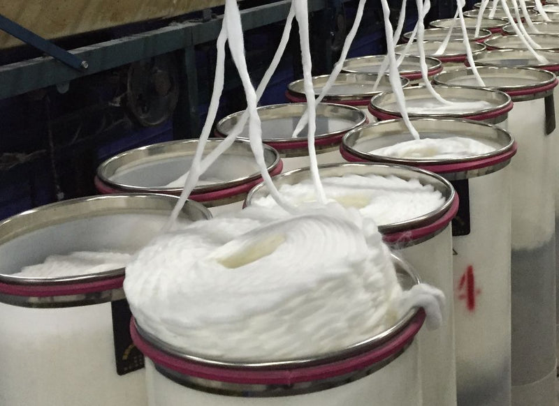 Large white spools of thick yarn or thread hanging from metal frames in an industrial setting.