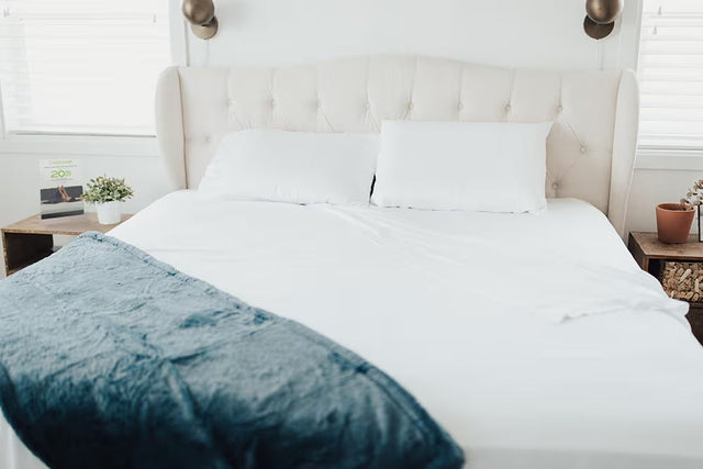 White tufted headboard bed dressed in crisp white Cariloha bamboo sheets with a folded teal throw, in a sunlit vacation rental bedroom in Albion, California