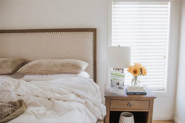 Vacation rental bed with a tan upholstered headboard dressed in white Cariloha bamboo sheets, beside a nightstand with a lamp and fresh sunflowers, in a Lake Arrowhead, California rental