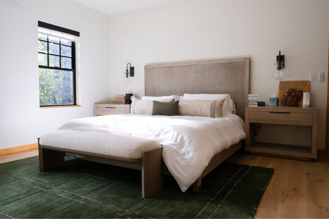 King bed with a wood-panel headboard dressed in white Cariloha bamboo bedding and a forest-green throw, in a guest room at Bandon Woods Resort