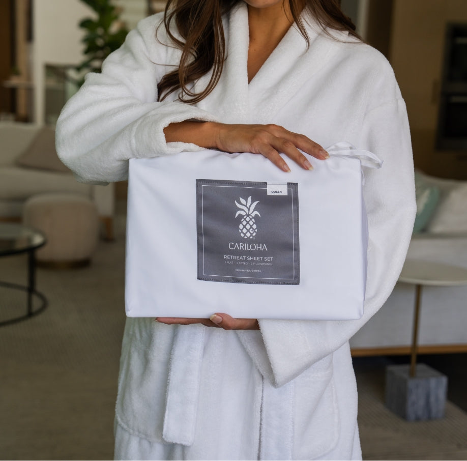 Woman in a Cariloha bamboo robe holding a wrapped Retreat Sheet Set gift package