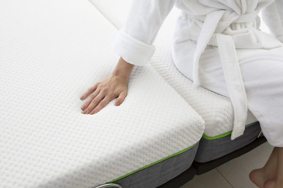 A close-up of a person in a white robe pressing down on a white textured Cariloha mattress to demonstrate its comfort and support.