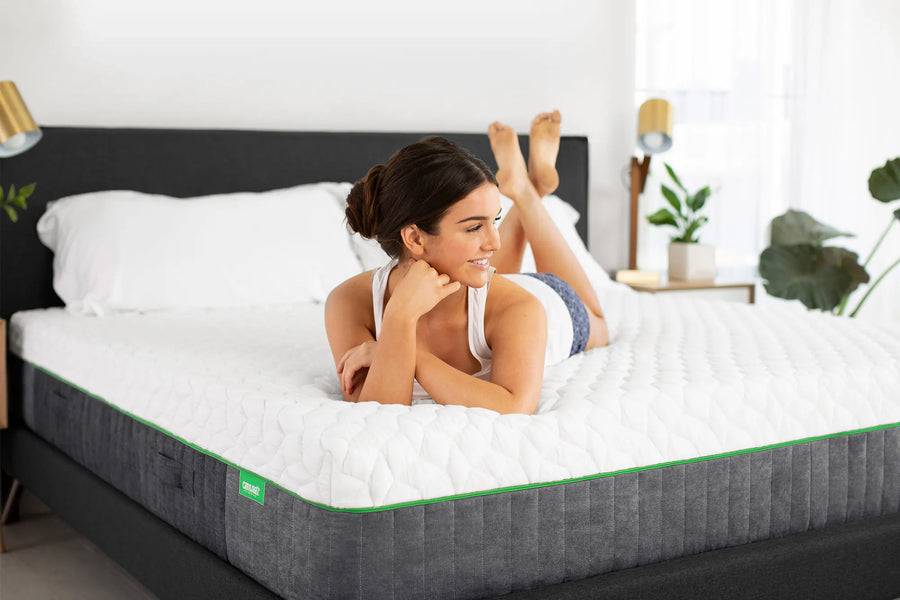 A woman lies on her stomach on a white quilted mattress topper on a cariloha resort mattress, in a bright, modern bedroom setting.