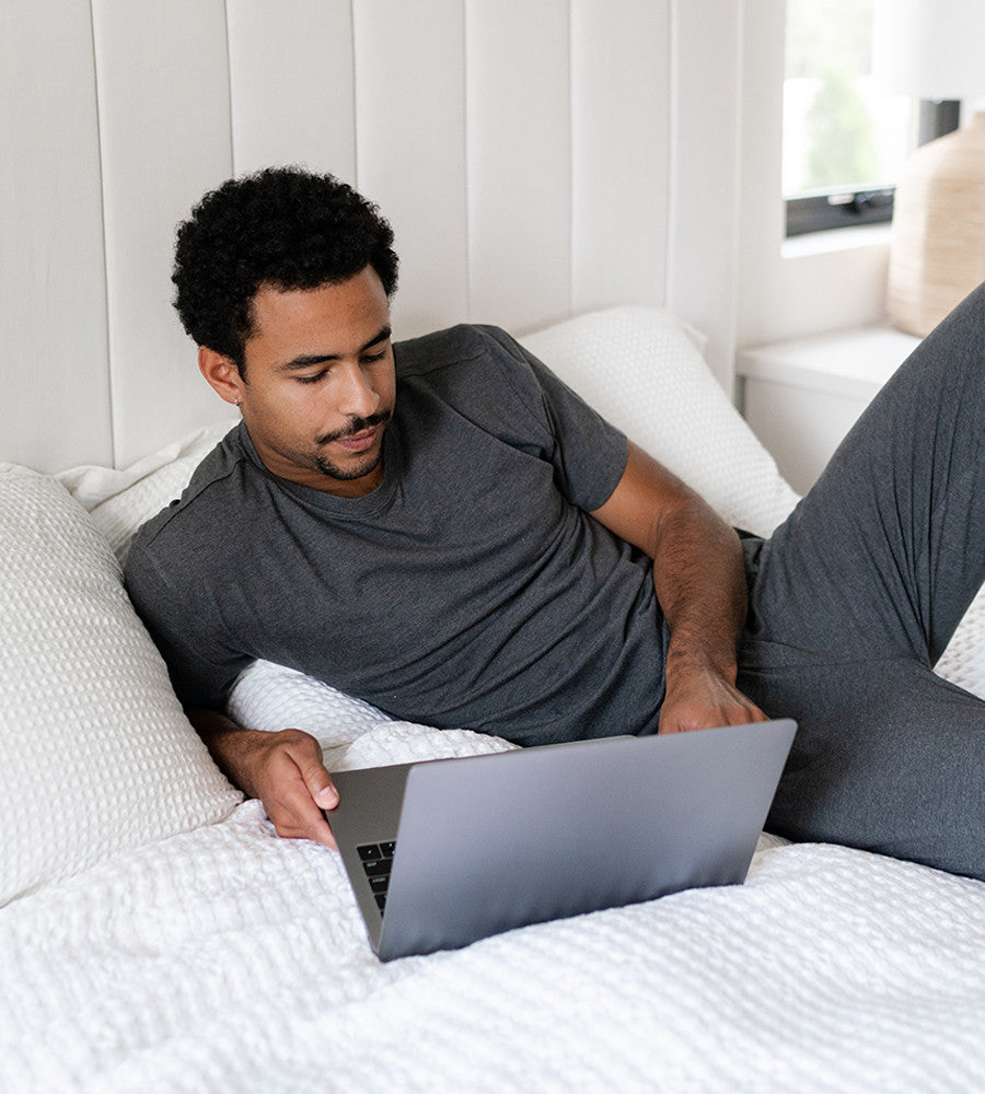 model lying on a bed wearing charcoal heather crew