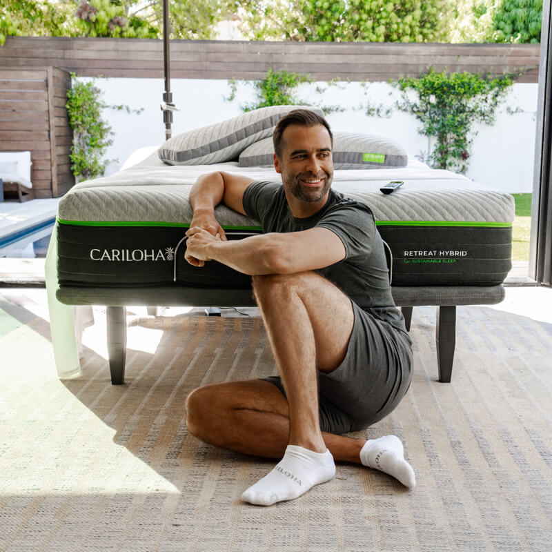 Man sitting beside the Cariloha Retreat Hybrid mattress on an outdoor patio bed frame