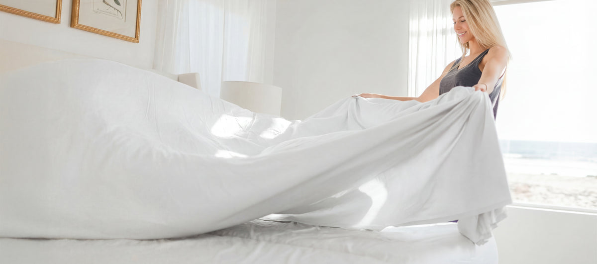 a woman making a bed with white cariloha bamboo sheets
