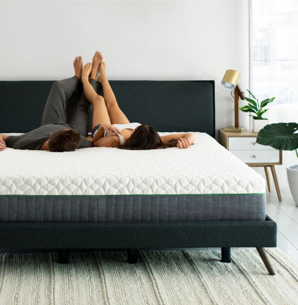 A couple lying on a white quilted mattress on a dark bed frame in a bright, modern bedroom.