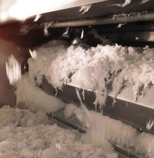 White fluffy bamboo fibers processing on a conveyor belt inside a machine, with some fibers flying in motion.