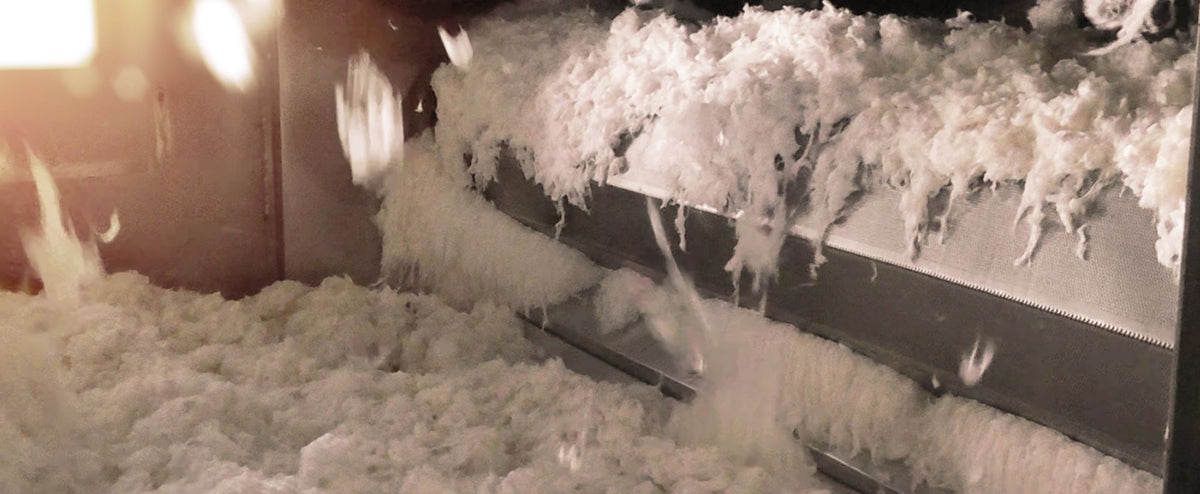 White fluffy bamboo fiber being processed on a conveyor belt, with some pieces falling in motion.