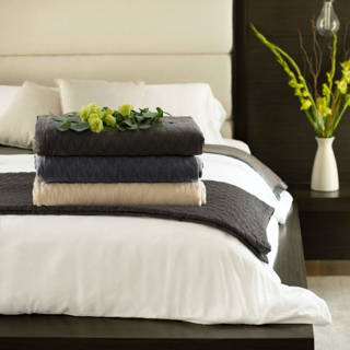 Stack of folded Cariloha bamboo throw blankets in charcoal and cream on a white bed