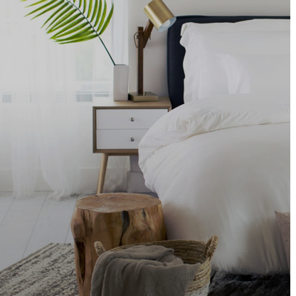 Bright bedroom corner styled with Cariloha bamboo bedding, a wood nightstand, potted palm, and a woven basket